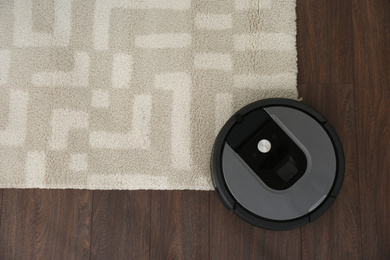 Modern robotic vacuum cleaner on wooden floor with carpet, top view. Space for text