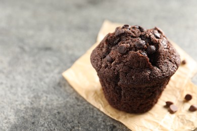 Photo of Delicious chocolate muffin on grey textured table, closeup. Space for text