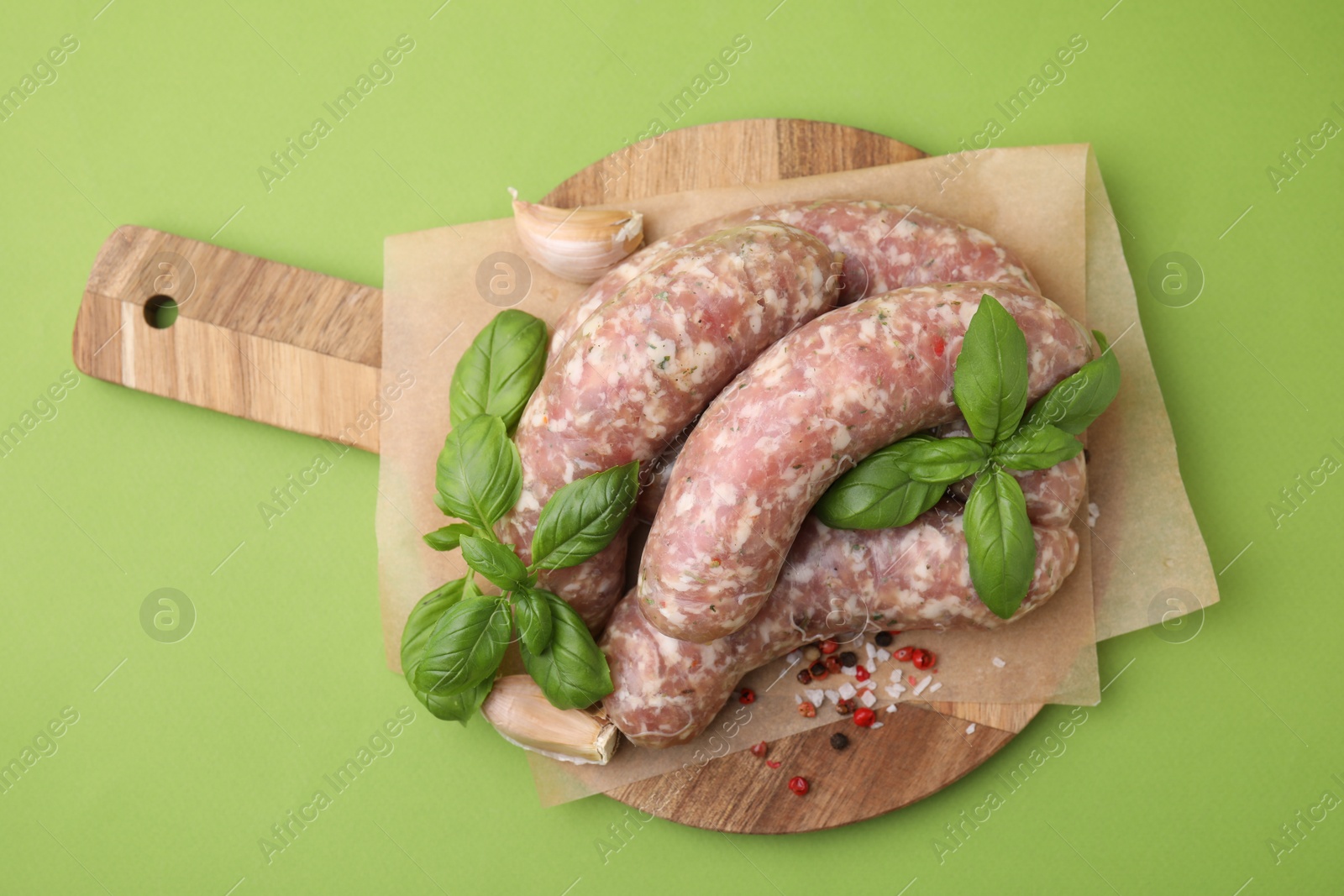 Photo of Raw homemade sausages and different spices on green background, top view