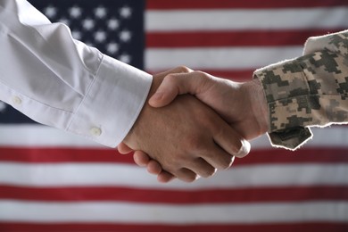 Photo of Soldier and businessman shaking hands against flag of USA, closeup