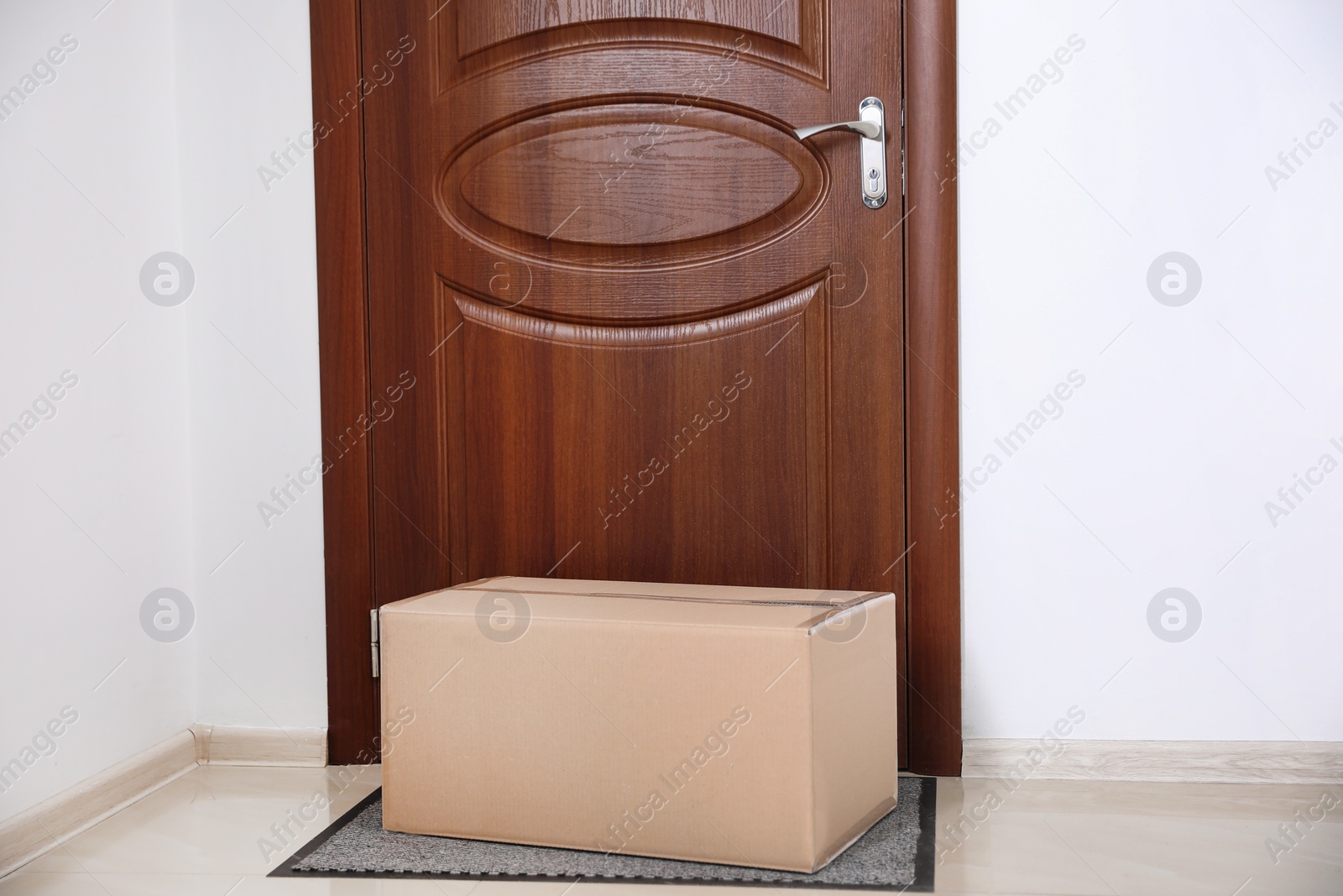 Photo of Cardboard box on rug near door. Parcel delivery service