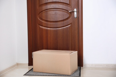 Photo of Cardboard box on rug near door. Parcel delivery service