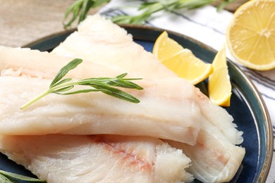 Photo of Pieces of raw cod fish, rosemary and lemon on table, closeup