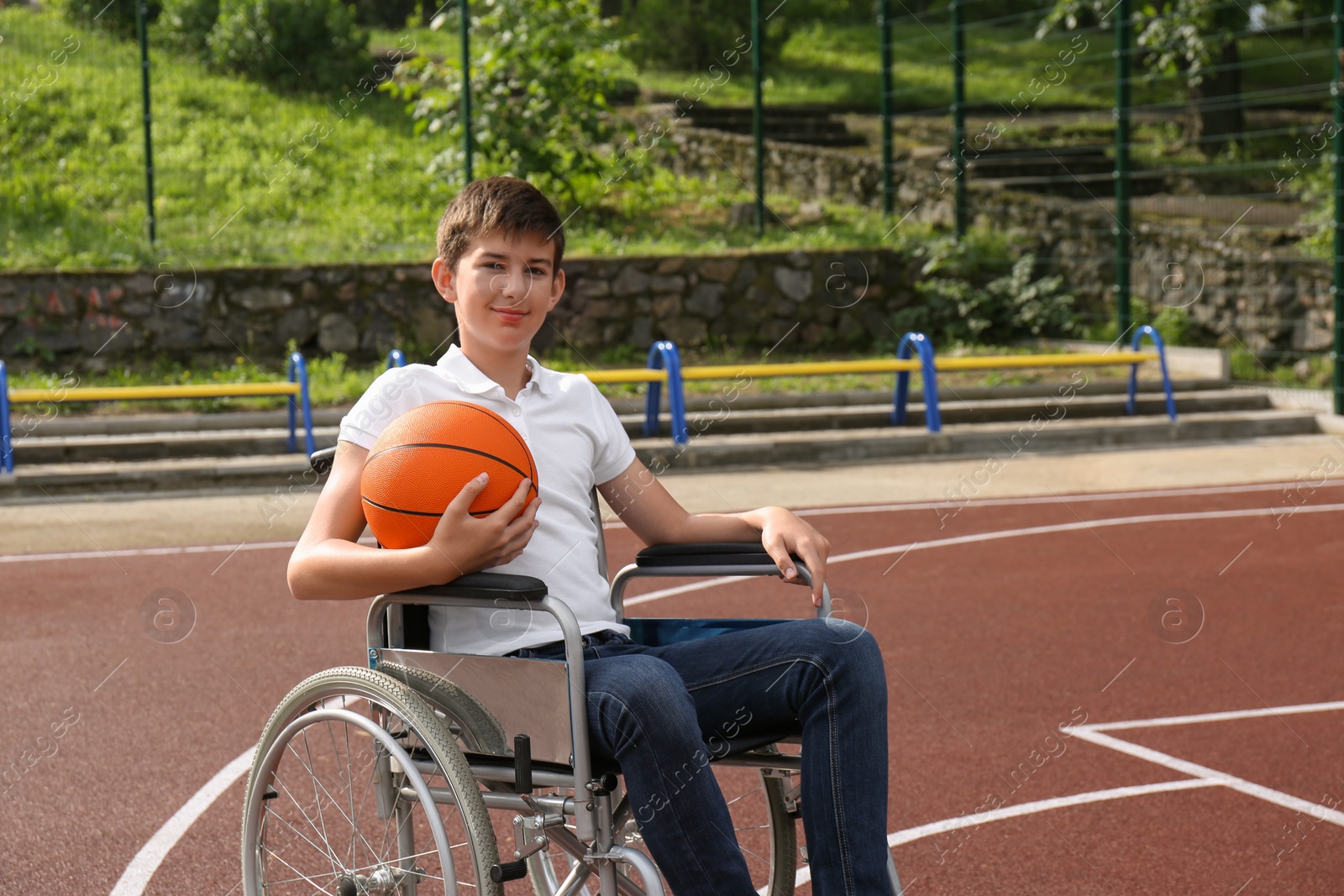 Photo of Disabled teenage boy in wheelchair with basketball ball at outdoor court