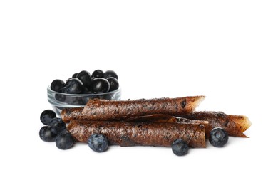 Delicious fruit leather rolls and blueberries on white background