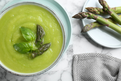 Delicious asparagus soup in bowl on white marble table, flat lay