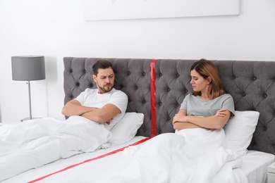 Photo of Upset couple with relationship problems lying separately in bed at home