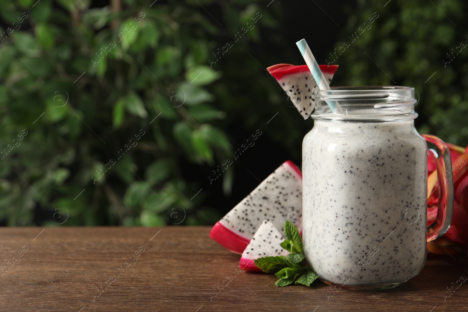 Photo of Delicious pitahaya smoothie in mason jar and fresh fruits on wooden table, space for text