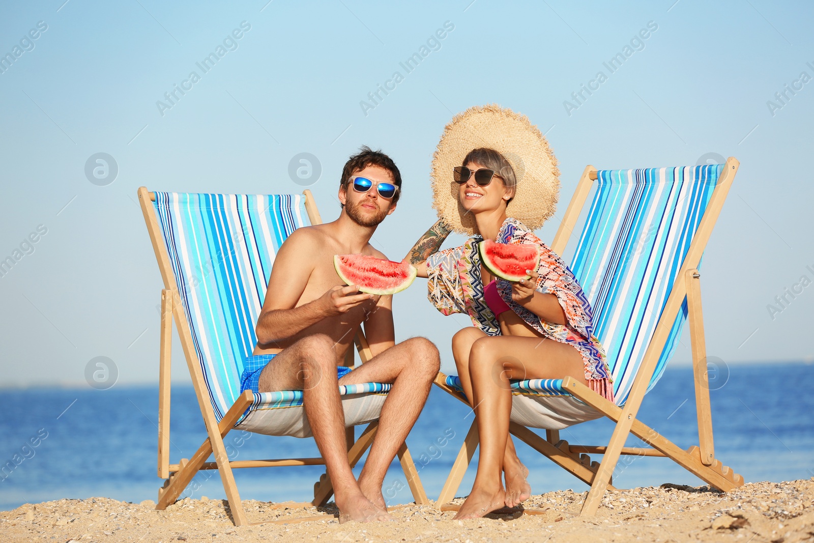 Photo of Young couple with watermelon slices in beach chairs at seacoast