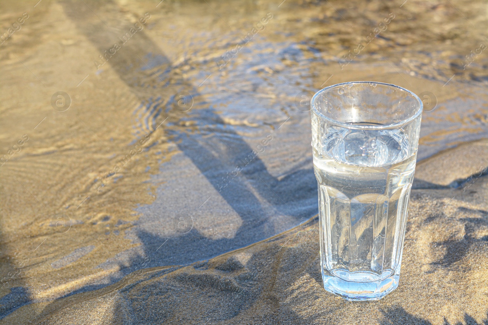 Photo of Glass of clean water on wet sand outdoors. Space for text