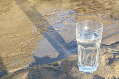 Photo of Glass of clean water on wet sand outdoors. Space for text