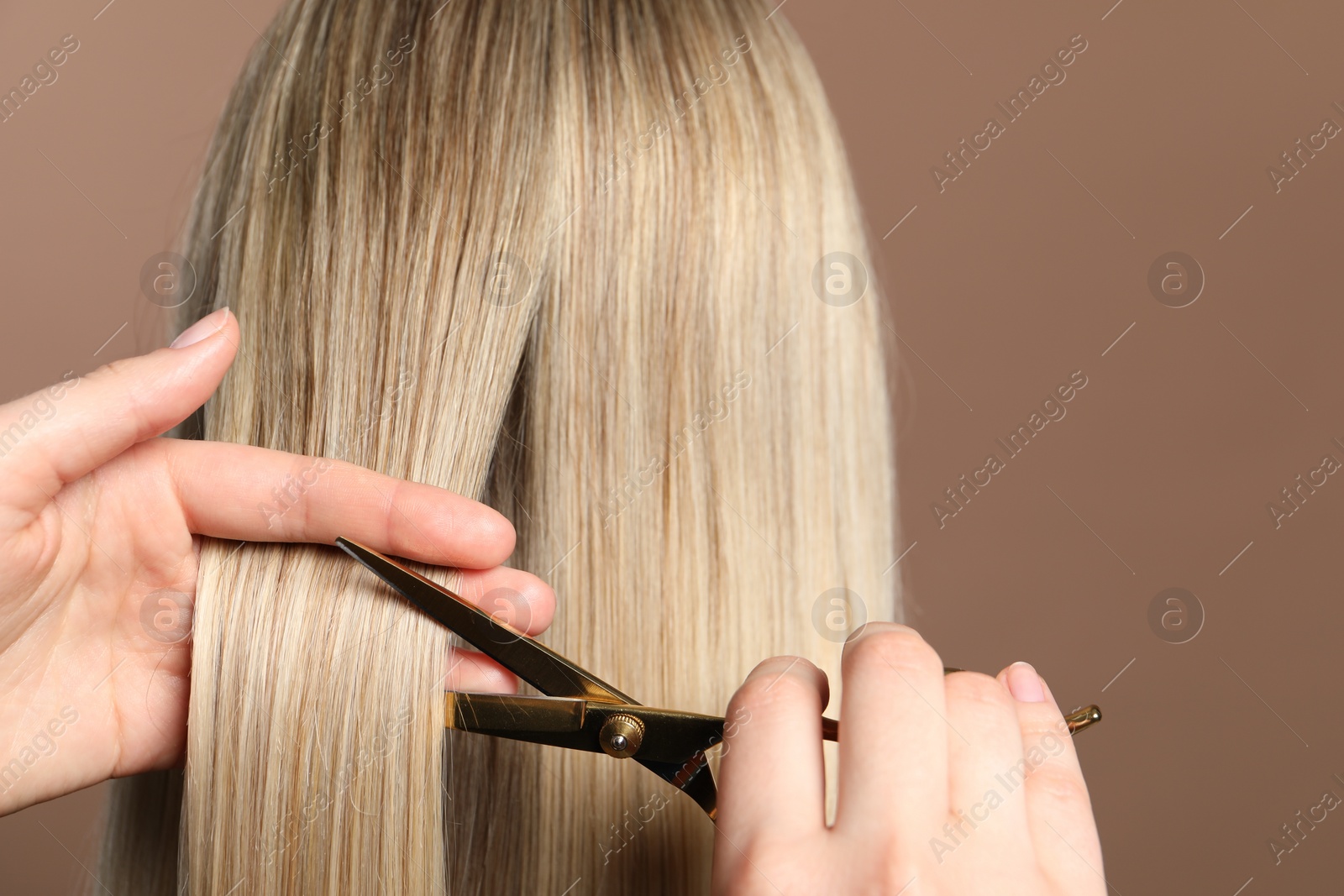 Photo of Hairdresser cutting client's hair with scissors on light brown background, closeup. Space for text