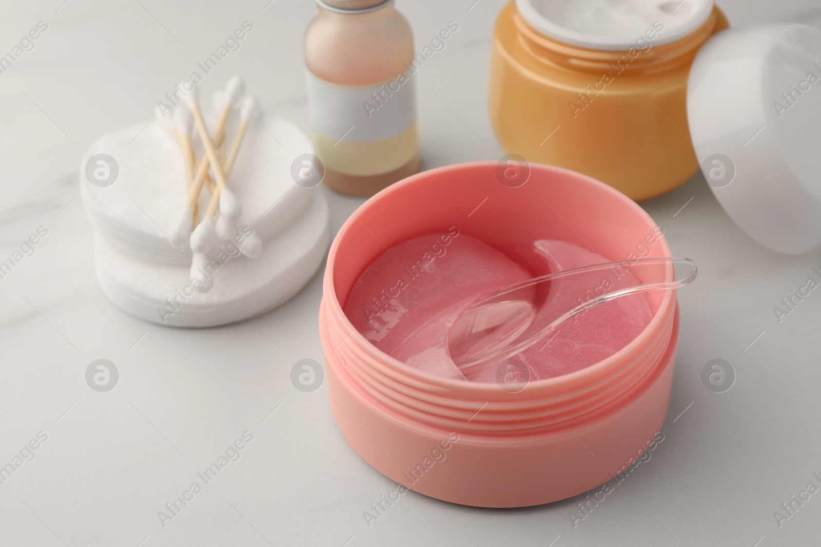 Photo of Jar of under eye patches with spoon and cosmetic products on white background, closeup