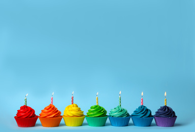 Photo of Delicious birthday cupcakes with burning candles on light blue background