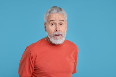 Portrait of surprised senior man on light blue background