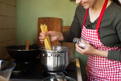 Photo of Woman cooking spaghetti on stove in kitchen, closeup