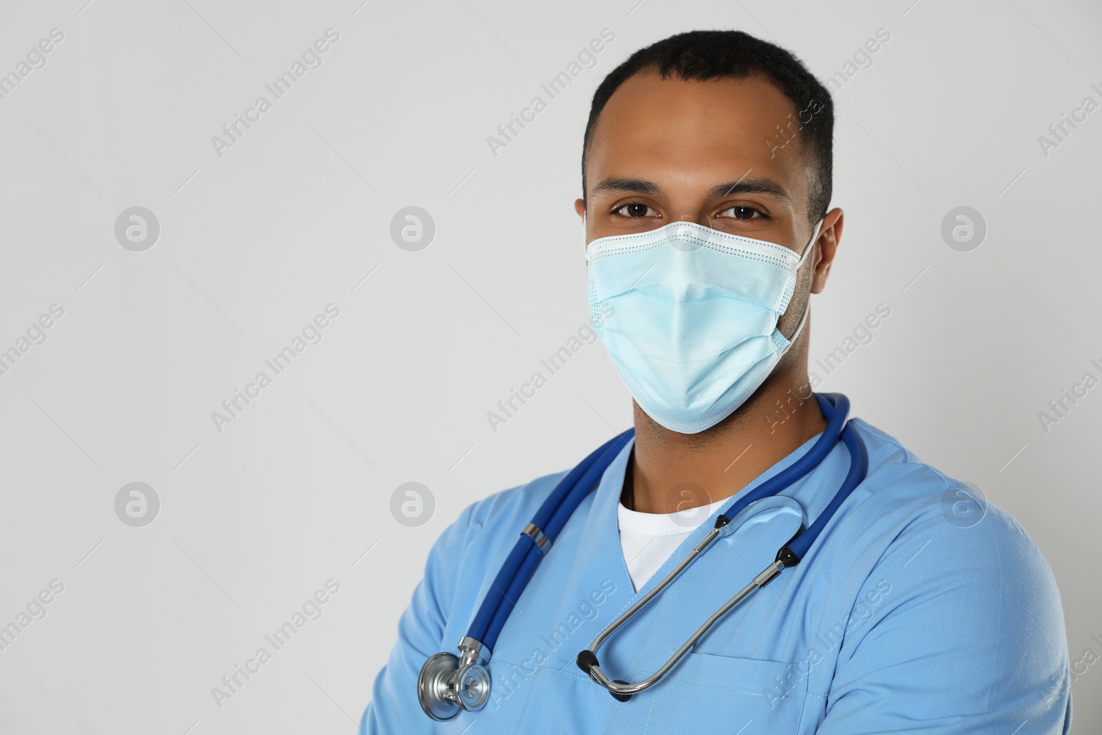 Photo of Doctor or medical assistant (male nurse) with protective mask and stethoscope on light grey background. Space for text