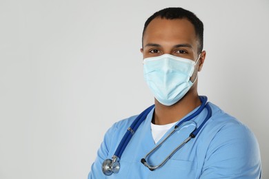 Photo of Doctor or medical assistant (male nurse) with protective mask and stethoscope on light grey background. Space for text
