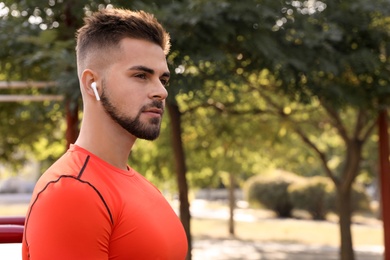 Young man with wireless headphones listening to music on sports ground. Space for text