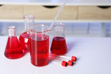 Photo of Laboratory analysis. Different glassware with red liquid on white table indoors. Space for text