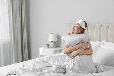 Photo of Beautiful woman hugging pillow on comfortable bed with silky linens, space for text