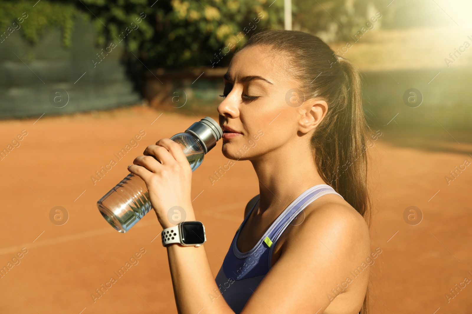 Photo of Woman with modern smart watch drinking water on tennis court