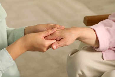 Young and elderly women holding hands indoors, closeup