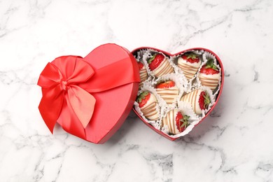 Photo of Heart shaped box with delicious chocolate covered strawberries on white marble table, top view