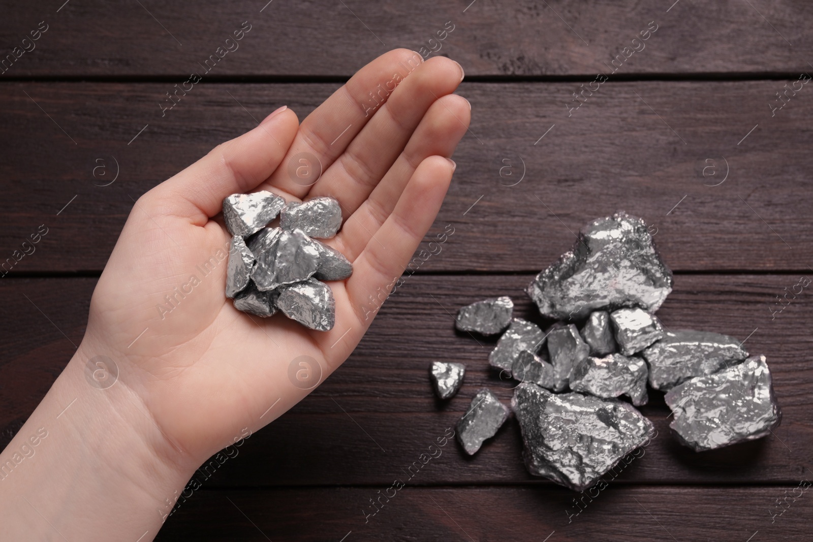 Photo of Woman with silver nuggets at wooden table, top view