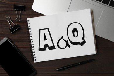 Photo of Notebook with text A&Q, laptop and smartphone on wooden table, flat lay