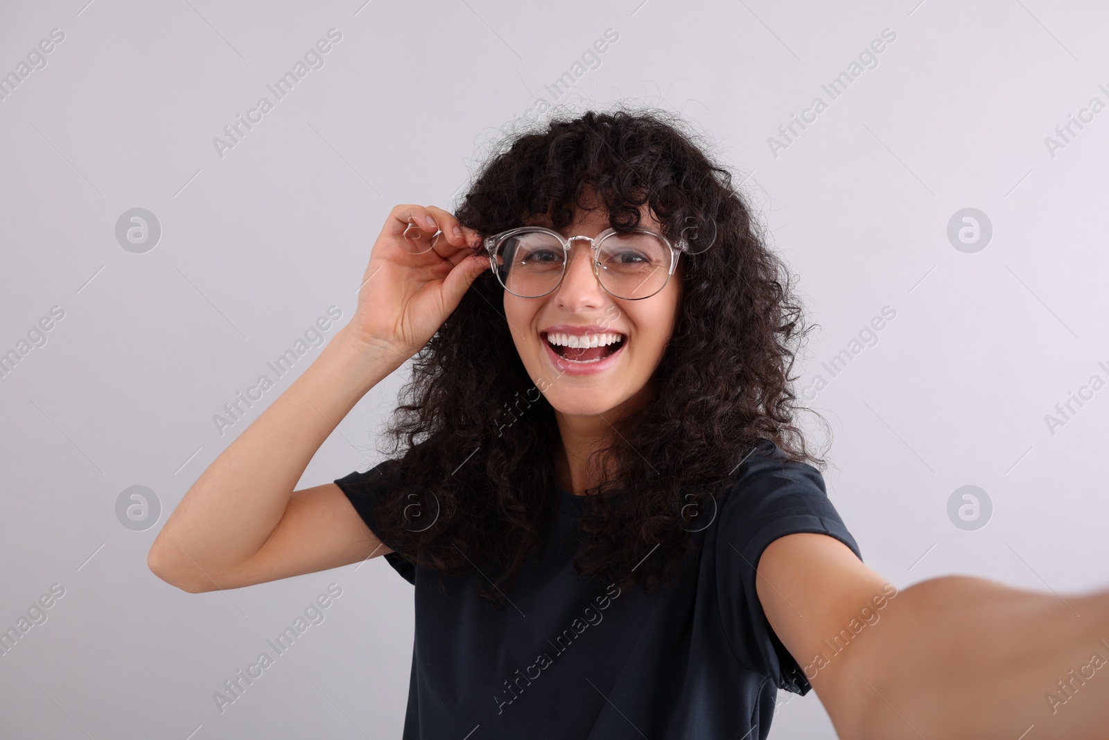 Photo of Beautiful young woman in eyeglasses taking selfie on light grey background