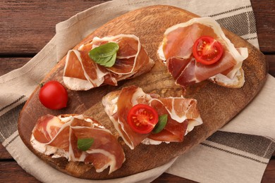 Photo of Board of tasty sandwiches with cured ham, basil and tomatoes on wooden table, top view