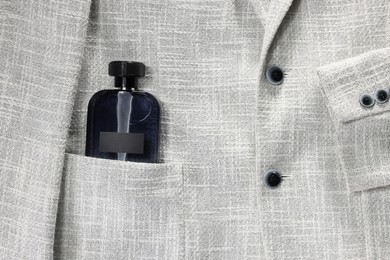 Photo of Luxury men's perfume in pocket of grey jacket, top view. Space for text