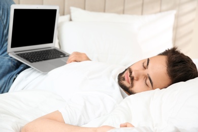 Photo of Lazy young man with laptop sleeping on bed at home