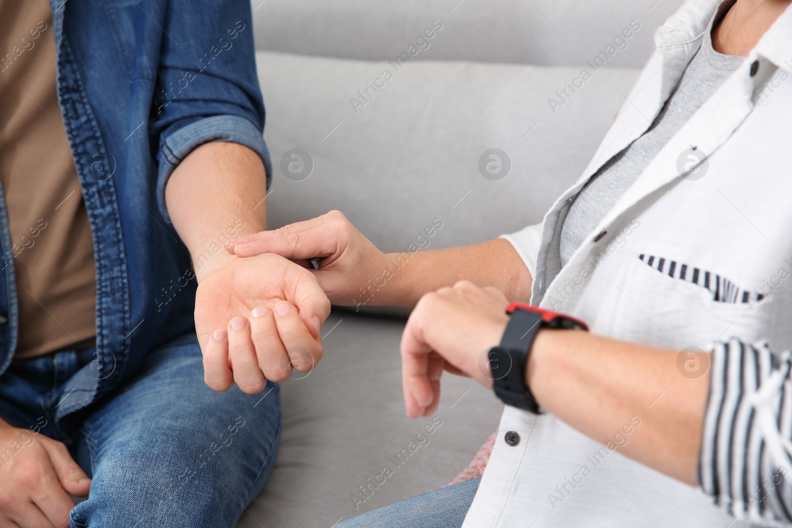 Photo of Mature woman checking man's pulse with fingers indoors, closeup