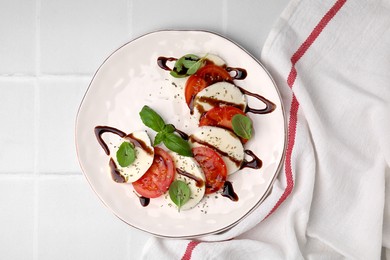 Photo of Delicious Caprese salad with balsamic vinegar on white tiled table, top view