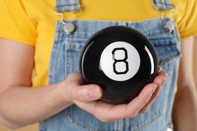 Photo of Woman holding magic eight ball on light brown background, closeup