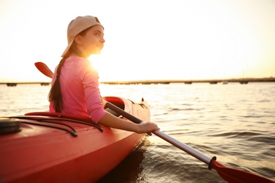 Happy girl kayaking on river at sunset. Summer camp activity