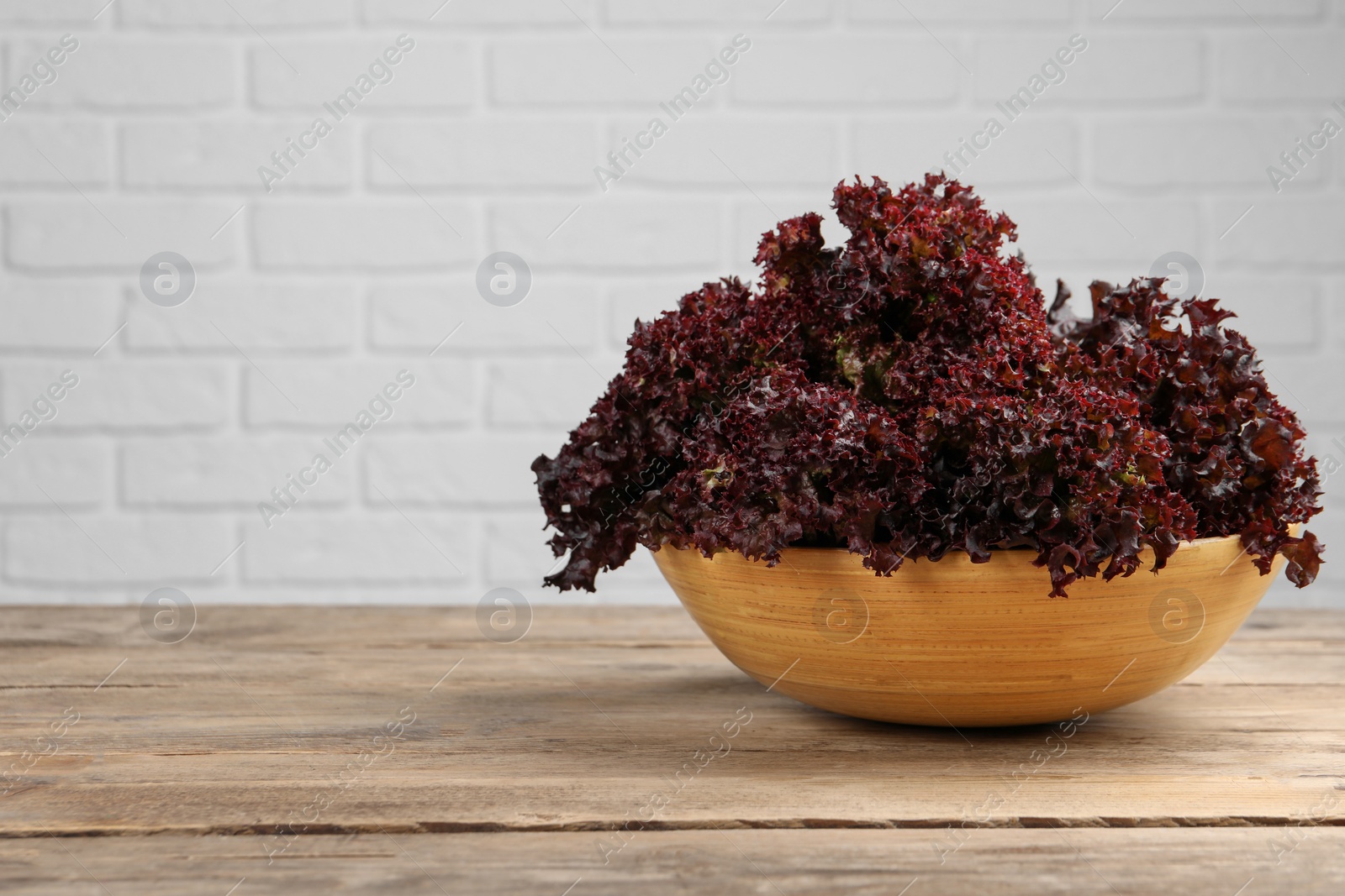 Photo of Bowl with fresh red coral lettuce on wooden table, space for text