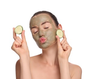 Beautiful woman with clay mask holding pieces of cucumber and blowing kiss on white background
