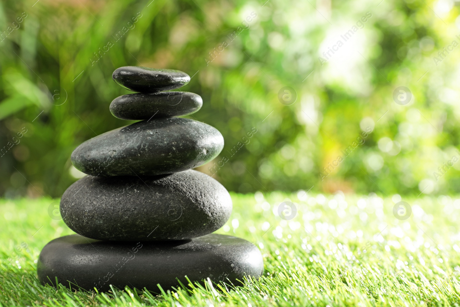 Photo of Stack of stones on green grass against blurred background, space for text. Zen concept