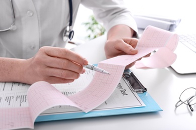 Doctor examining cardiogram at table in clinic, closeup