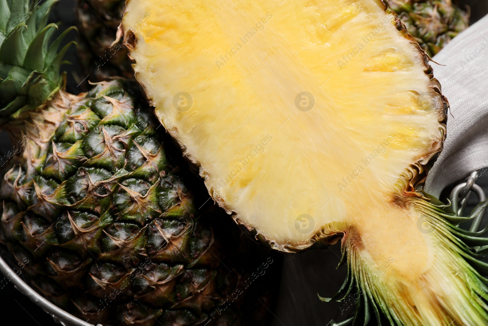 Photo of Whole and cut ripe pineapples in metal basket on table, flat lay