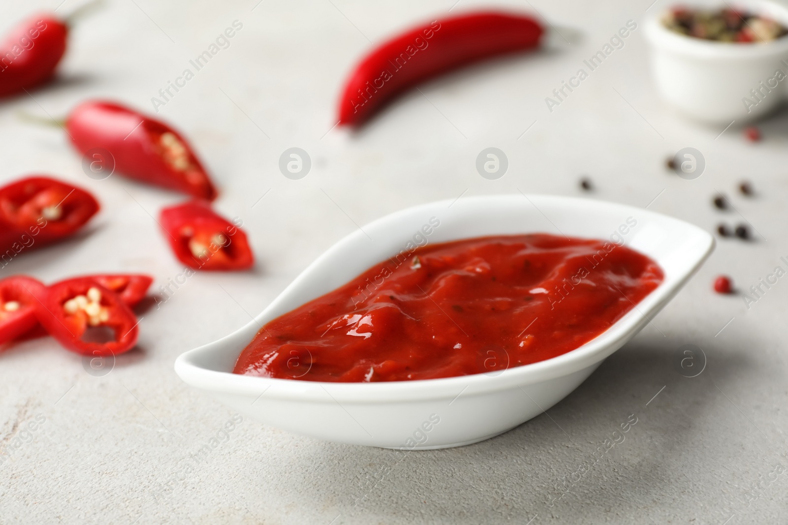 Photo of Gravy boat with spicy chili sauce on light table