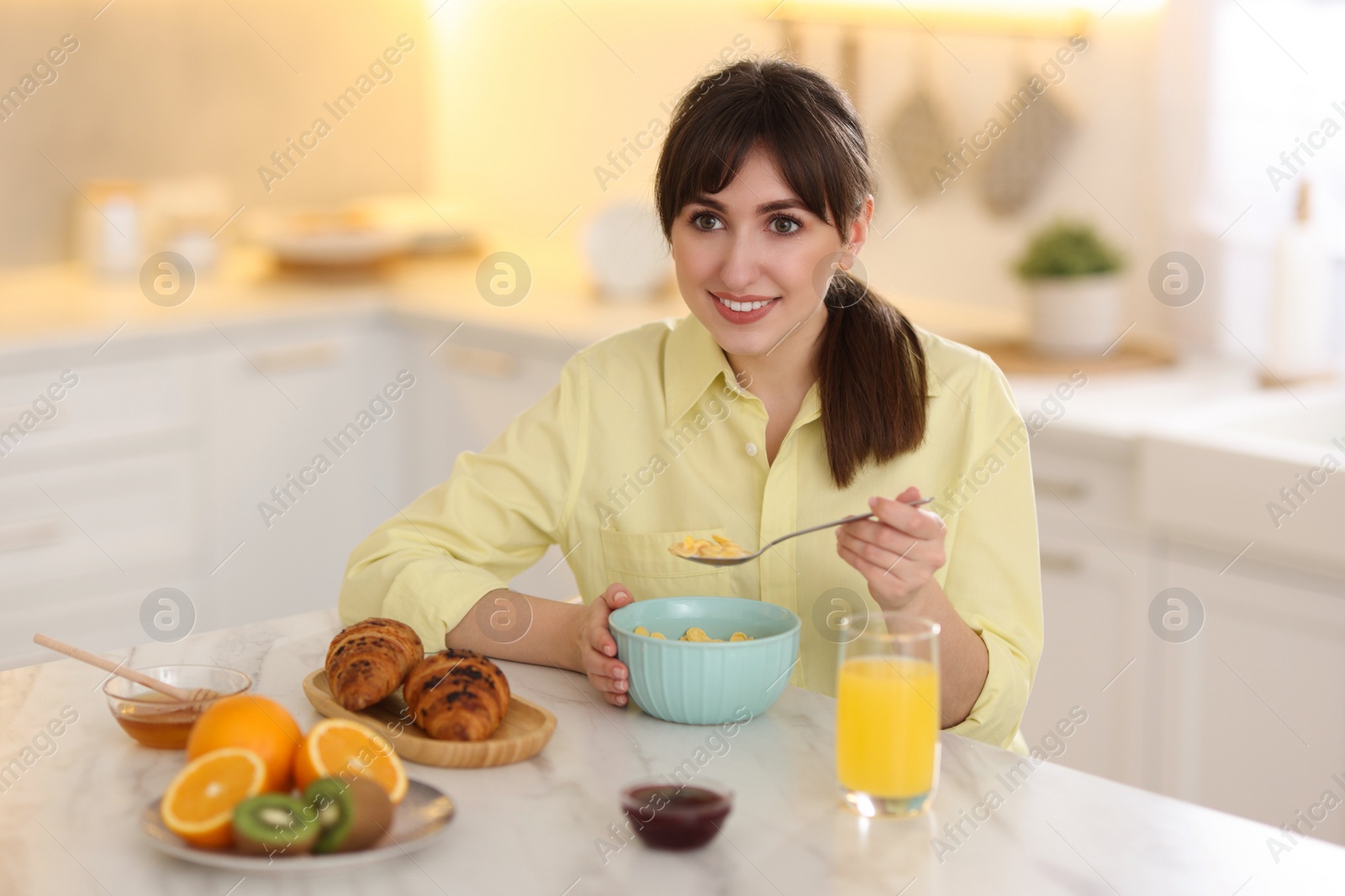 Photo of Smiling woman eating tasty cornflakes at breakfast indoors