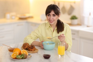 Photo of Smiling woman eating tasty cornflakes at breakfast indoors