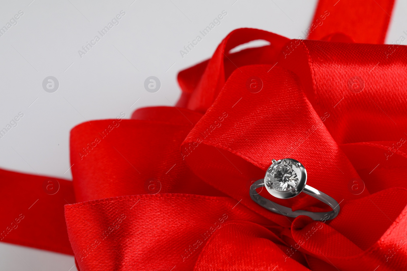 Photo of Beautiful red bow and engagement ring on white background, closeup