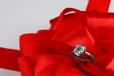 Photo of Beautiful red bow and engagement ring on white background, closeup