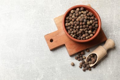 Photo of Aromatic allspice pepper grains in bowl and scoop on grey table, top view. Space for text
