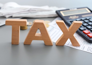 Photo of Word TAX and calculator on table, closeup